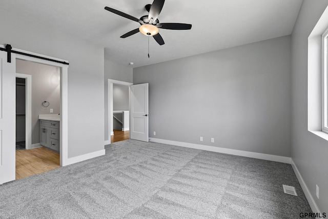 unfurnished bedroom with carpet, baseboards, a barn door, visible vents, and a ceiling fan