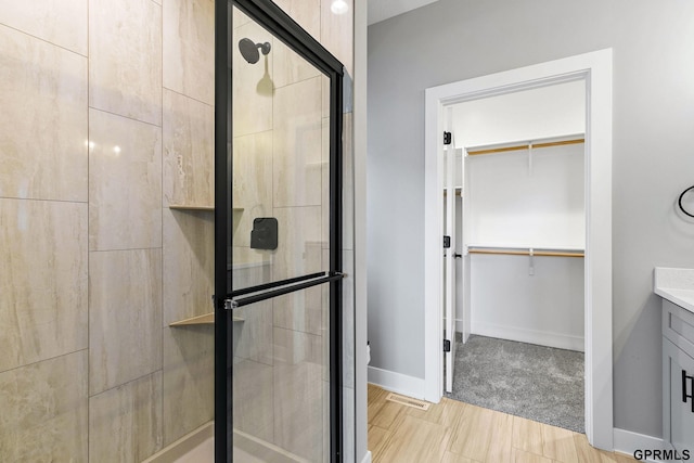 bathroom featuring baseboards, a stall shower, a spacious closet, and vanity