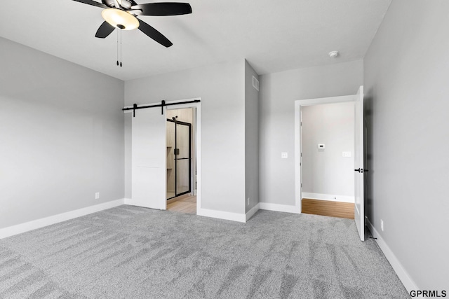unfurnished bedroom with baseboards, carpet floors, a barn door, visible vents, and a ceiling fan