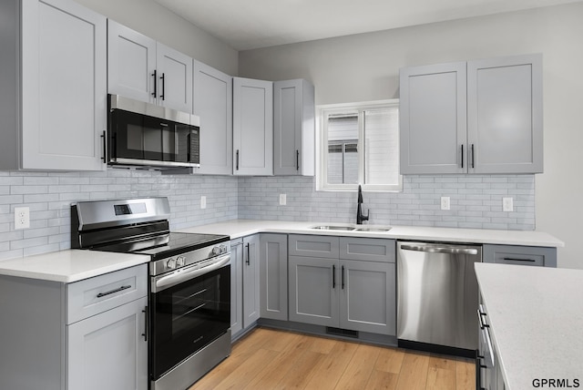 kitchen with gray cabinetry, light wood-type flooring, light countertops, stainless steel appliances, and a sink