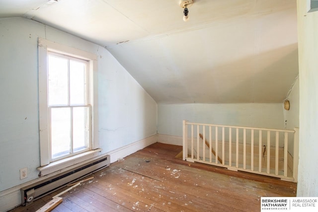 additional living space with vaulted ceiling, a healthy amount of sunlight, hardwood / wood-style floors, and a baseboard radiator