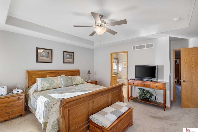 bedroom with a tray ceiling, light colored carpet, visible vents, and connected bathroom