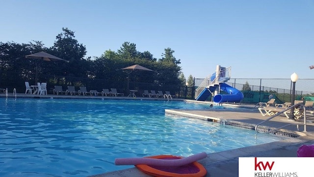 community pool featuring a patio area, a water slide, and fence