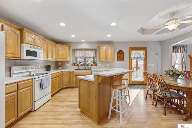 kitchen featuring a sink, a kitchen breakfast bar, white appliances, and a wealth of natural light