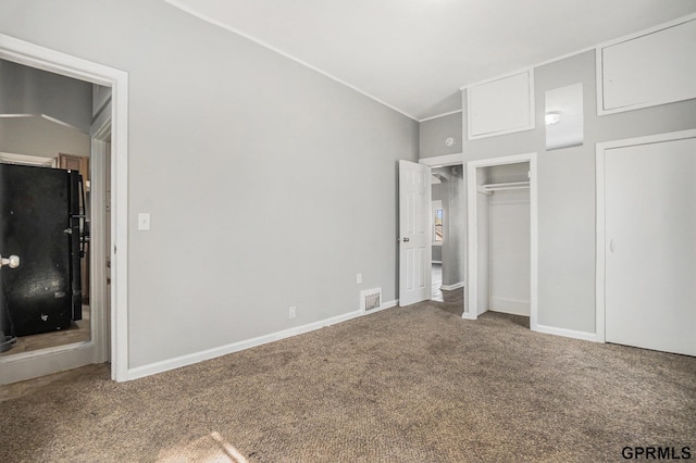 unfurnished bedroom with visible vents, baseboards, freestanding refrigerator, lofted ceiling, and carpet floors