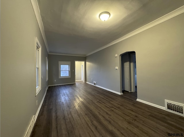 unfurnished room with dark wood-style floors, visible vents, baseboards, arched walkways, and crown molding