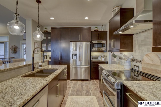 kitchen featuring a sink, hanging light fixtures, stainless steel appliances, wall chimney exhaust hood, and backsplash