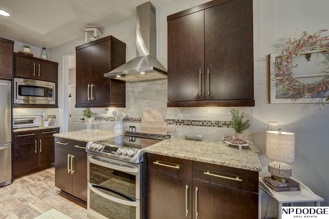 kitchen with light stone counters, stainless steel appliances, dark brown cabinetry, wall chimney range hood, and decorative backsplash