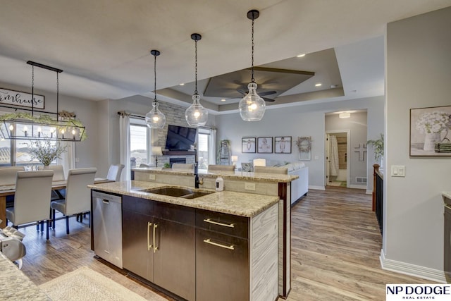 kitchen with open floor plan, a tray ceiling, stainless steel dishwasher, light wood-style floors, and a sink