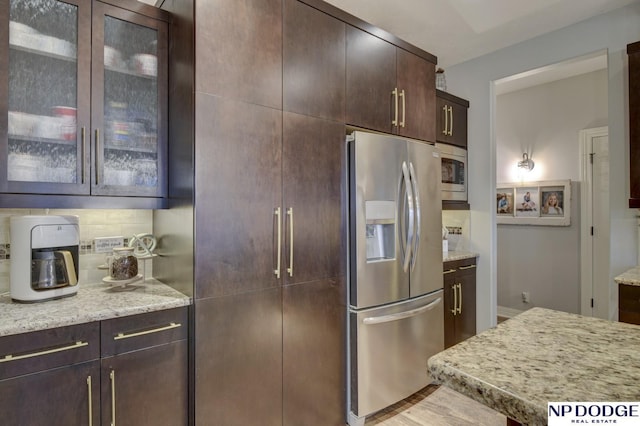 kitchen featuring dark brown cabinets, glass insert cabinets, light stone countertops, and appliances with stainless steel finishes