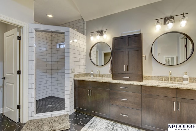 bathroom featuring double vanity, a tile shower, and a sink