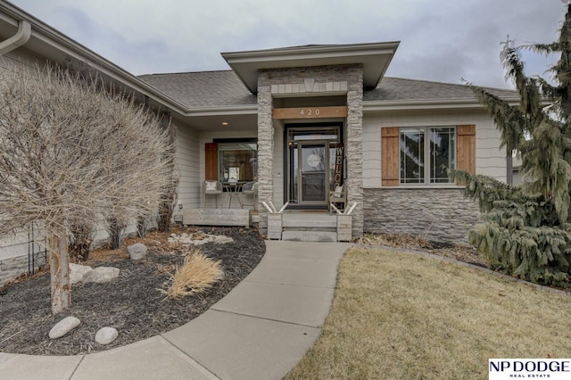 view of exterior entry with stone siding and roof with shingles