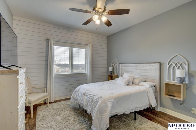 bedroom featuring wooden walls, a ceiling fan, baseboards, and wood finished floors