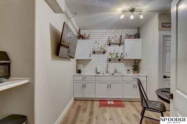 bar with backsplash, baseboards, light wood-style floors, a textured ceiling, and a sink