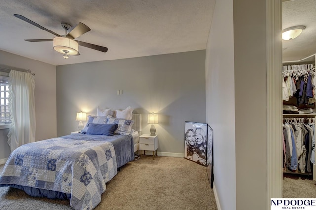 bedroom featuring a walk in closet, a textured ceiling, a closet, carpet flooring, and baseboards