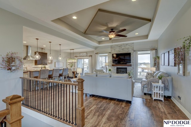 living room featuring a ceiling fan, a tray ceiling, a healthy amount of sunlight, and dark wood-style flooring