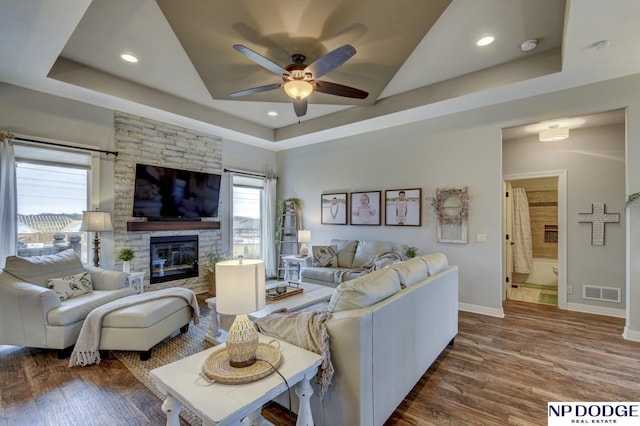 living room featuring a tray ceiling, wood finished floors, a ceiling fan, and visible vents