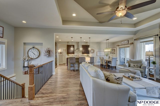 living room with a ceiling fan, a raised ceiling, recessed lighting, and wood finished floors