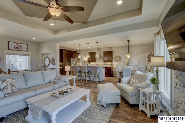 living area with recessed lighting, a ceiling fan, a tray ceiling, and dark wood-style flooring