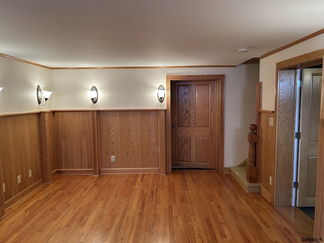 interior space featuring a wainscoted wall, wood walls, light wood-type flooring, and ornamental molding