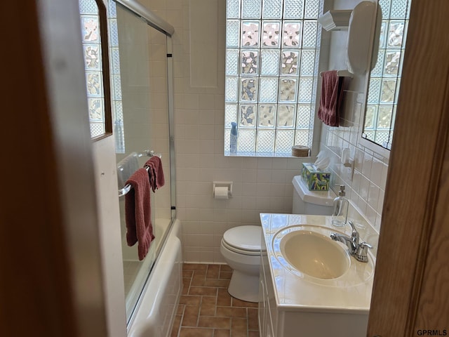 full bath featuring combined bath / shower with glass door, toilet, tile walls, and vanity