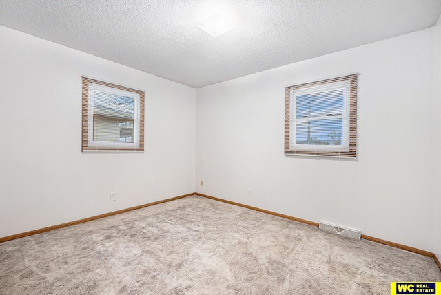 carpeted spare room with visible vents, baseboards, and a textured ceiling