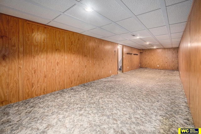 finished below grade area with carpet flooring, a paneled ceiling, and wooden walls