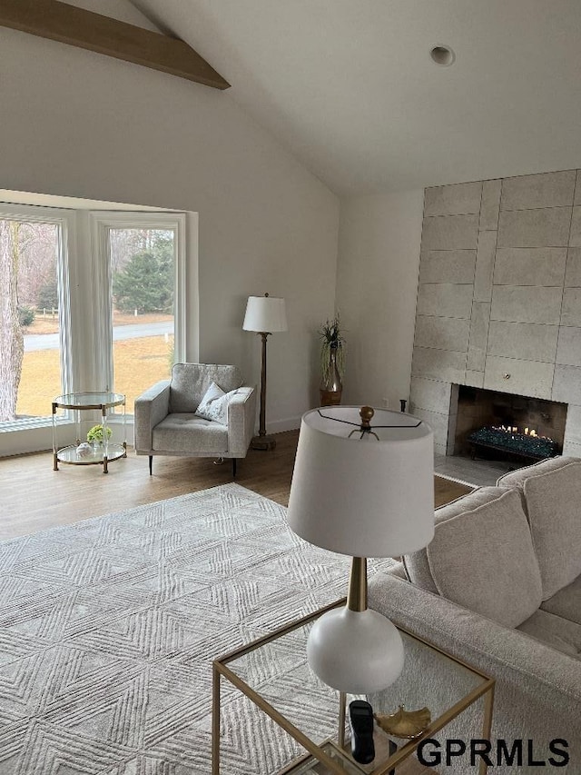 living area with a tiled fireplace, vaulted ceiling, and wood finished floors