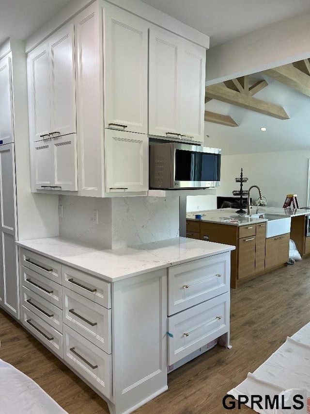 kitchen featuring light stone counters, stainless steel microwave, tasteful backsplash, dark wood-style floors, and white cabinetry