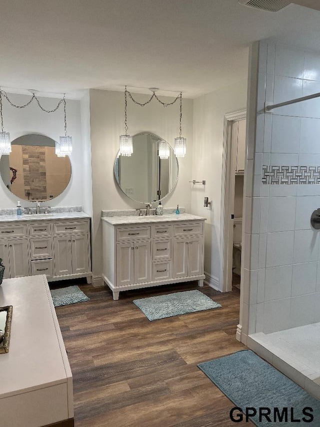 full bath featuring a tile shower, wood finished floors, and a sink