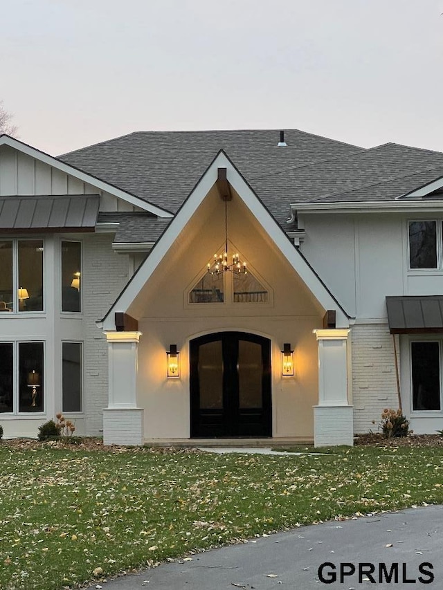 property entrance featuring a yard, brick siding, board and batten siding, and a shingled roof