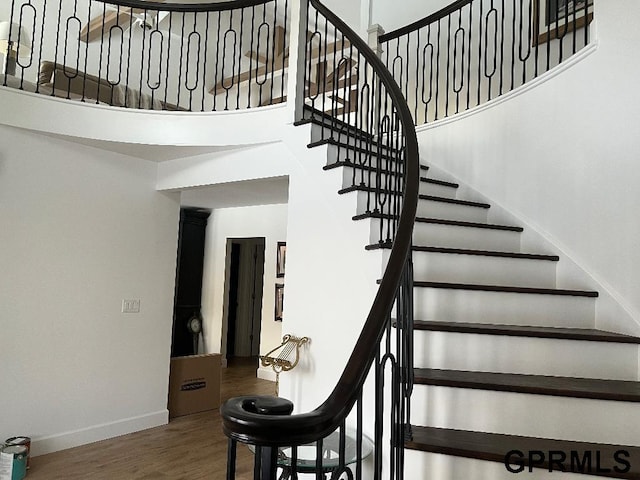 stairway with baseboards, a towering ceiling, and wood finished floors