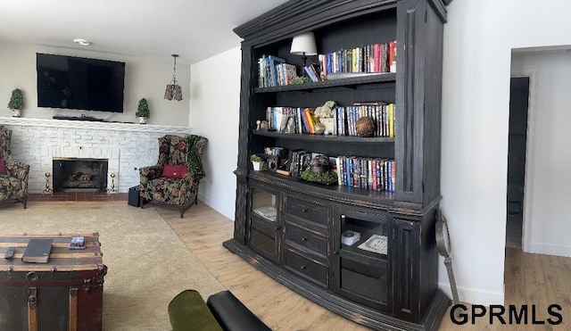 living room featuring baseboards, a brick fireplace, and wood finished floors