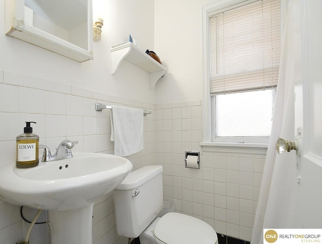 bathroom with a wainscoted wall, toilet, tile walls, and a sink