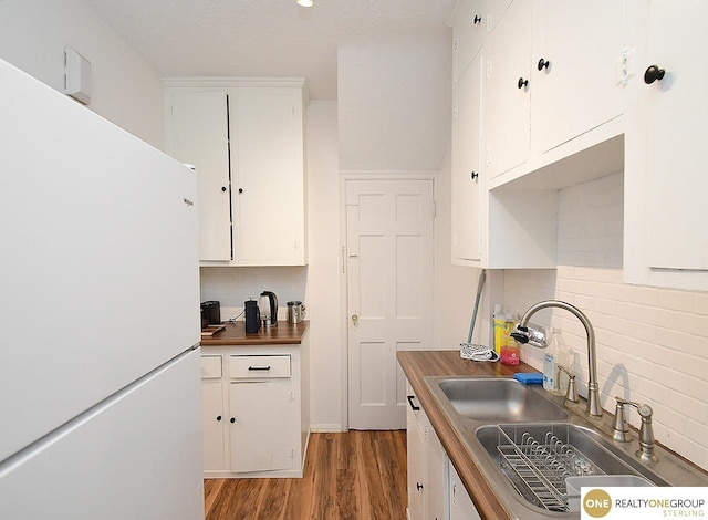 kitchen featuring tasteful backsplash, freestanding refrigerator, wood finished floors, white cabinets, and a sink