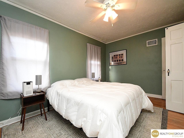 bedroom featuring crown molding, wood finished floors, visible vents, and a textured ceiling