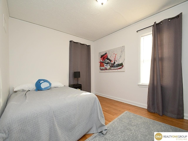 bedroom with a textured ceiling, light wood-type flooring, and baseboards