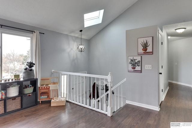 corridor featuring lofted ceiling with skylight, wood finished floors, an upstairs landing, and baseboards