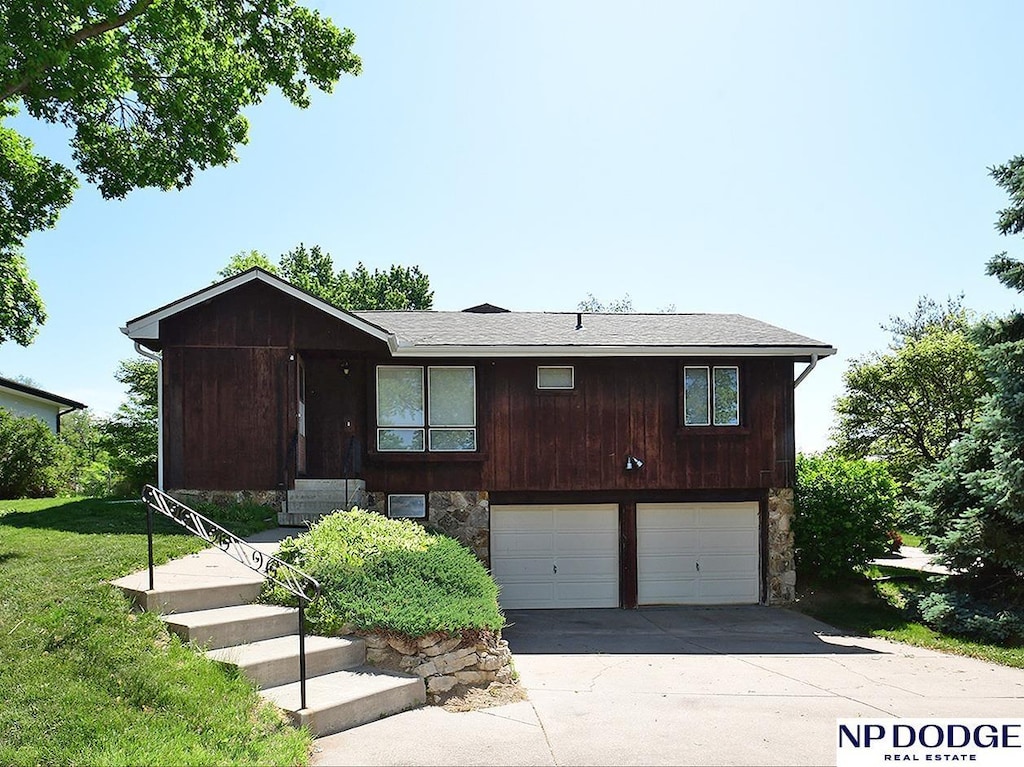 view of front of house with an attached garage, stone siding, concrete driveway, and a front yard