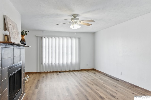 unfurnished living room with a ceiling fan, a fireplace, wood finished floors, baseboards, and a textured ceiling
