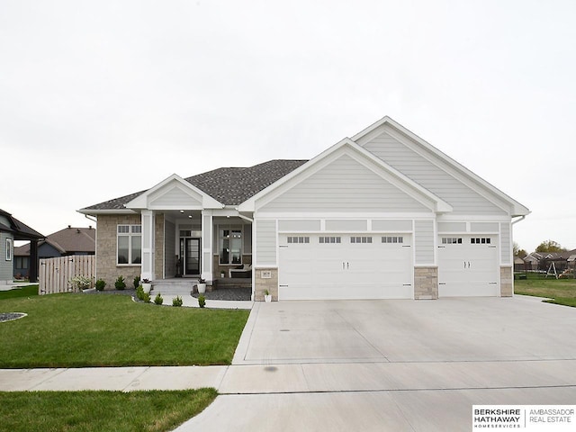 view of front of property with a front yard, roof with shingles, an attached garage, concrete driveway, and stone siding