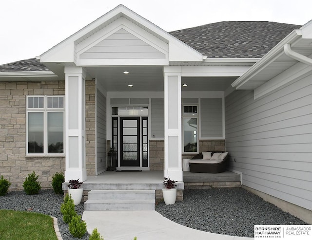 doorway to property featuring a porch, stone siding, and roof with shingles