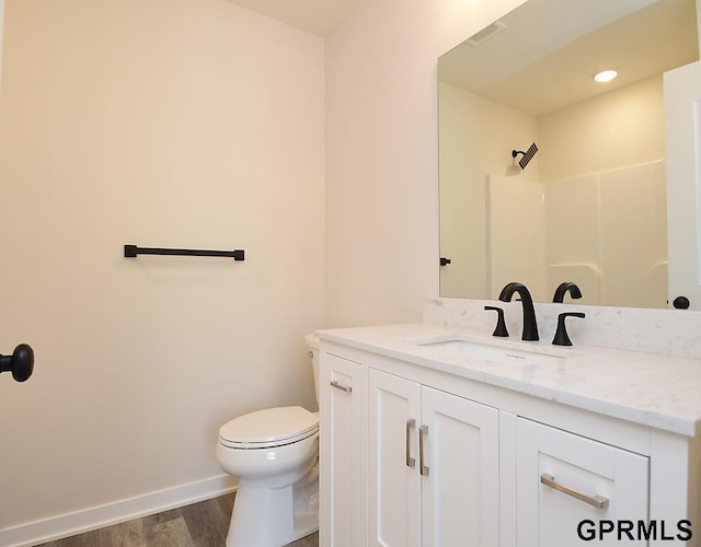 full bath with vanity, wood finished floors, baseboards, walk in shower, and toilet