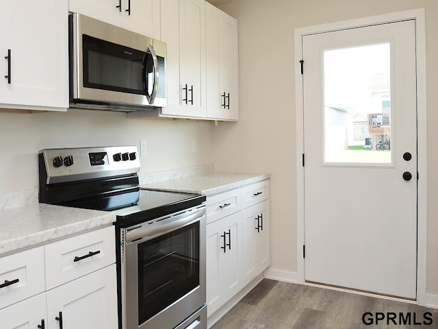 kitchen featuring light wood-style flooring, light stone counters, white cabinets, and appliances with stainless steel finishes