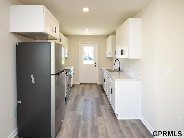 kitchen with a sink, wood finished floors, stainless steel appliances, white cabinets, and light countertops