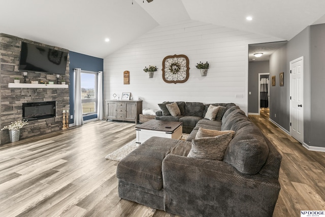 living area with ceiling fan, a stone fireplace, wood finished floors, and vaulted ceiling