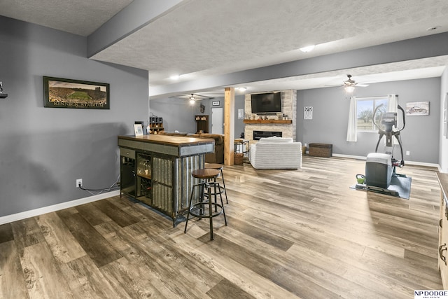 bar with wood finished floors, a textured ceiling, a stone fireplace, and ceiling fan