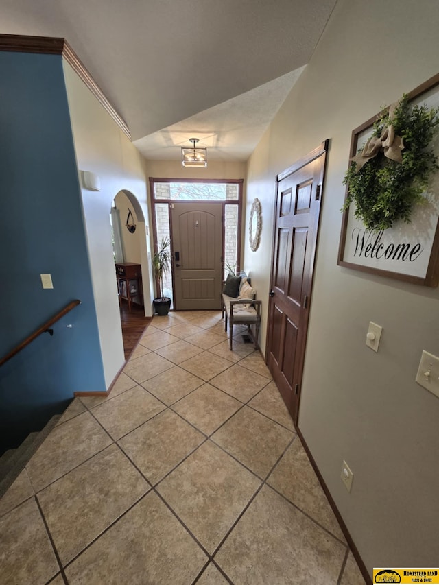 foyer with arched walkways, light tile patterned floors, and baseboards