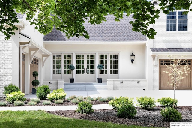 entrance to property featuring brick siding, french doors, and roof with shingles