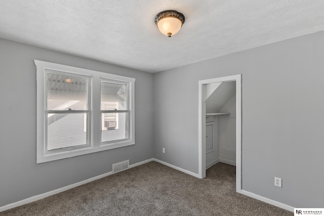 unfurnished bedroom with a closet, baseboards, carpet floors, a walk in closet, and visible vents
